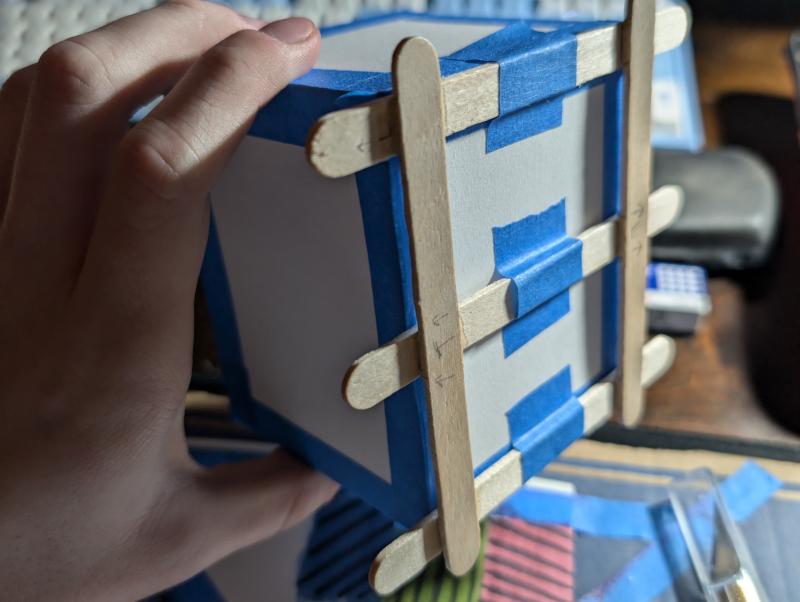Popsicle sticks around a paper box beginning to form the Deckbox's body