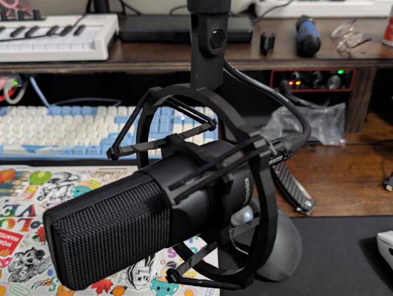 Two concentric rings connected via a leg with an elastic band with a microphone in the center suspended on a microphone arm